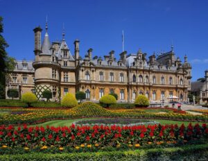 Waddesdon manor backed by a blue sky, with a formal garden in the foreground full of red flowers.