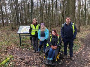 A group of people smiling and wearing high visibility vests about to go on a woodland walk at Brush Hill Nature Reserve