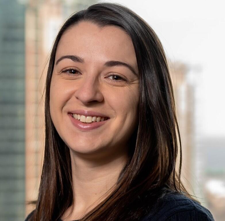 Photo of a woman with brown hair standing in front of a window.