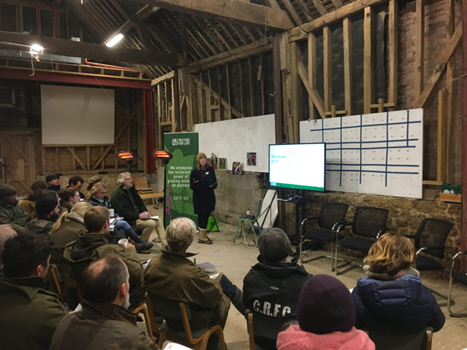 A group of people sit in a barn and watch a presentation.