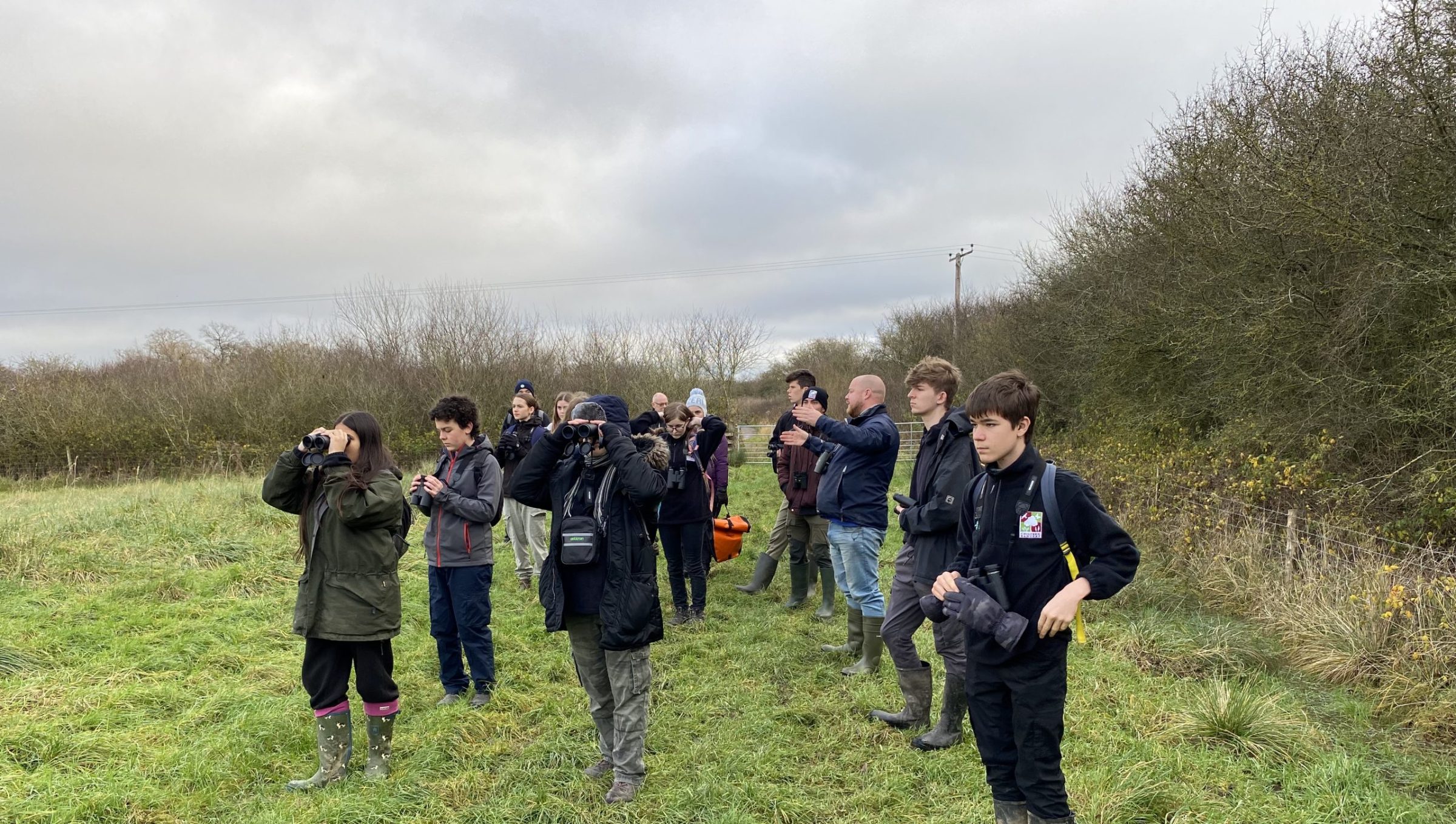 A group of young people bird watching in a field.