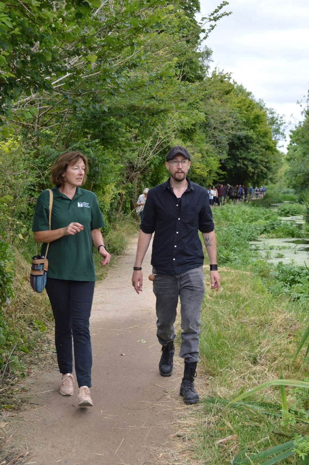 A woman and a man walk on a footpath alongside a canal.