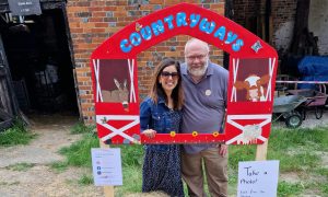 A woman and a man stand behind a sign shaped like a barn with the words "Countryways".