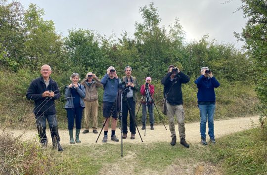 group of people looking through binoculars straight at the camera in a rural setting